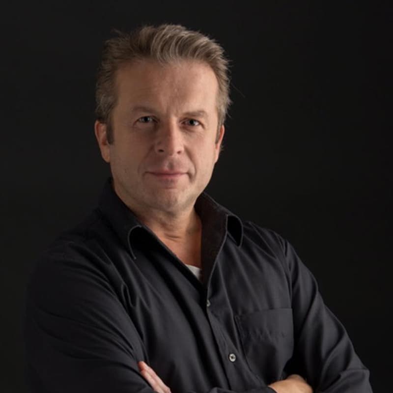 conductor Johannes Vogel wearing a black shirt with his arms crossed