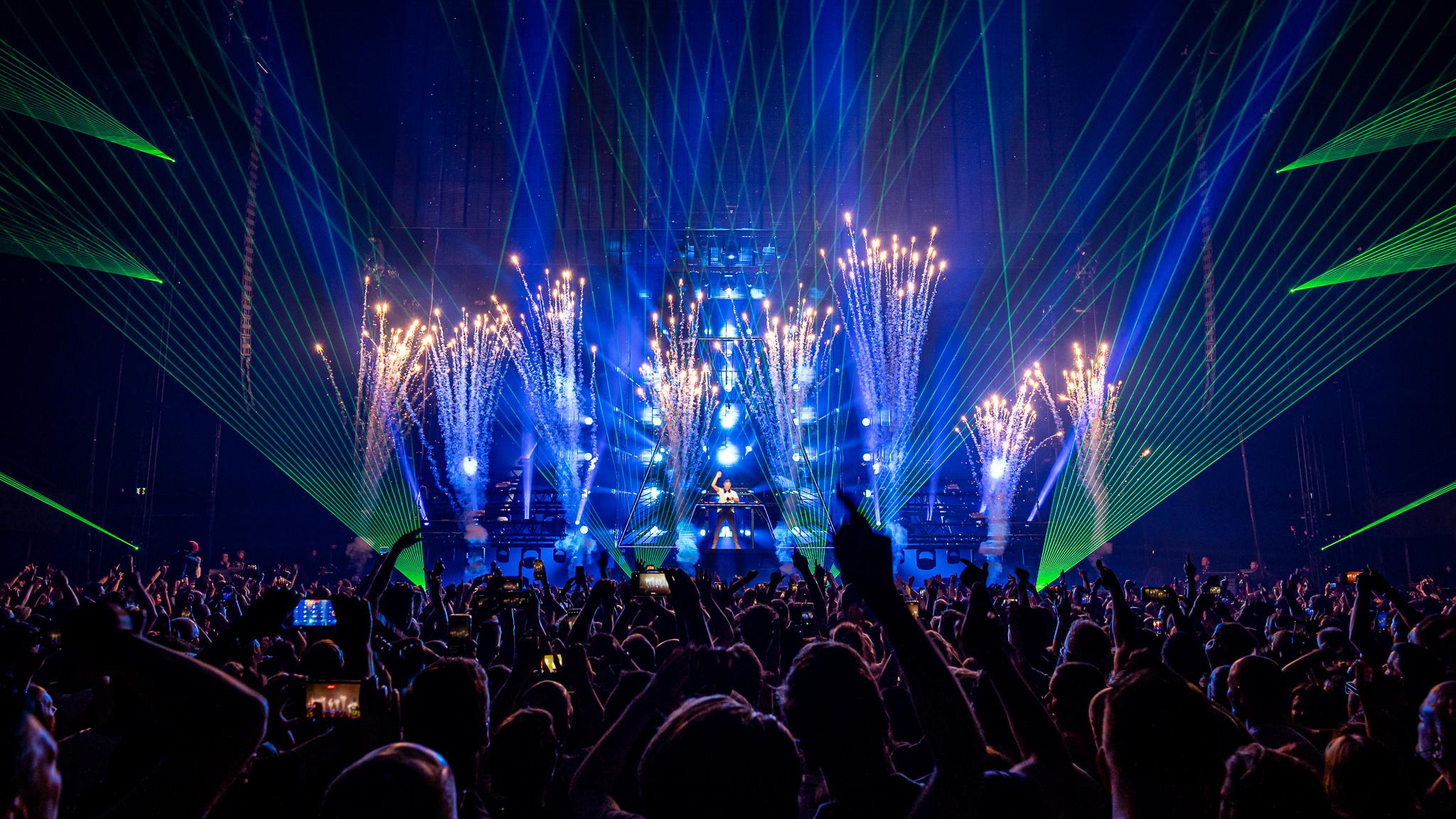 Armin van Buuren fans with their hands in the air as green and blue lasers soar over their heads 