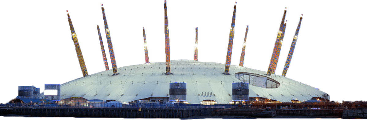 The 02 Arena London building with yellow support pylons is illuminated at night against a blue sky, with buildings visible in the background.