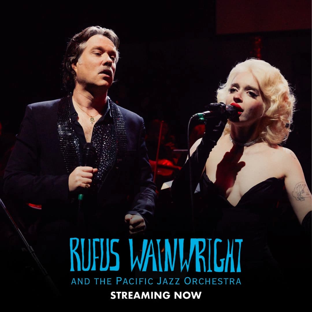 Rufus Wainwright performs on stage with microphones, dressed in formal black attire, under dramatic lighting. Text promotes "Rufus Wainwright: Wainwright Does Weill, Streaming Now.